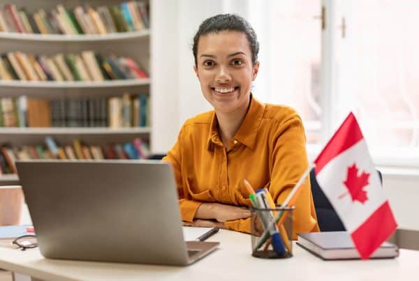 Online Foreign Languages Tutoring Happy Female Teacher Sitting Library With Flag Canada Using Laptop 600x403